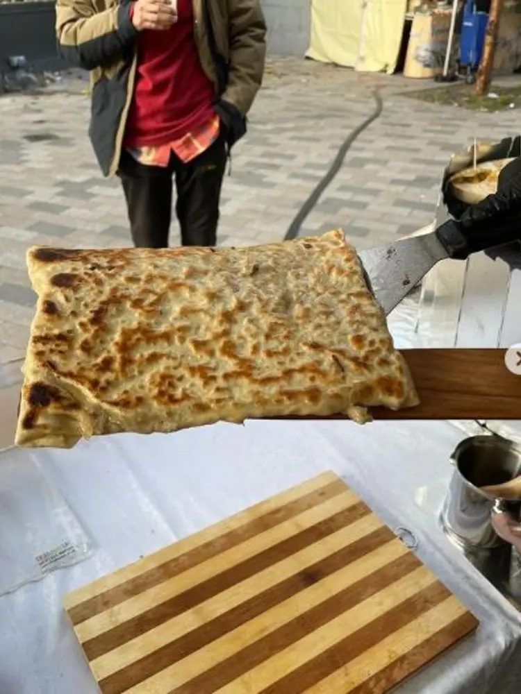 A whole gozleme flatbread lifted on a wooden peel at the stall counter