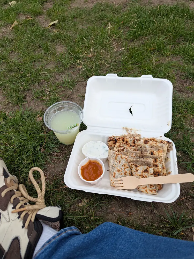 Gozleme slices in a takeaway box with garlic yoghurt, chilli sauce and a cup of lemonade